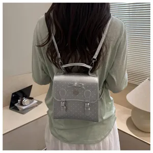 Detailed shot of a stylish silver polka dot mini backpack with cute bow and heart charm on model.