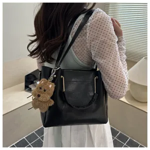 Detailed view of a trendy black leather bucket shoulder bag with a cute plush pendant.