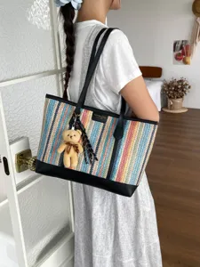 Woven tote bag detail view, showing colorful stripes, black leather trim and cute bear charm.