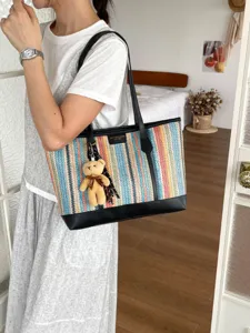 Detailed view of the colorful woven tote bag featuring black leather trim and a cute teddy bear.