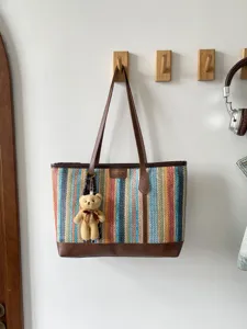 Woven tote bag detail showcasing multicolored striped texture and brown leather trim handles.