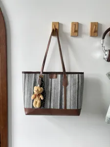 Woven tote bag with brown leather trim and cute bear pendant, stylish commuter shoulder bag.