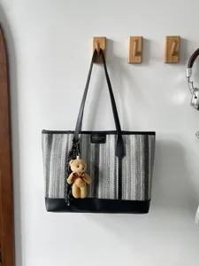 Detail shot of the black and white woven tote bag hanging on a hook with cute bear pendant.