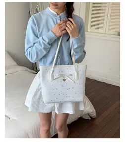 Detailed view of white star print tote bag with cute bow and heart charm, held by model.