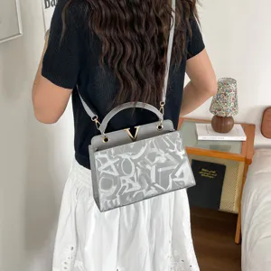 Detail view of stylish grey shoulder bag featuring gold V hardware and graphic pattern.