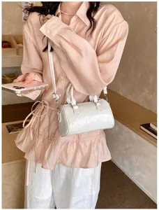 Chic white patent leather cylinder crossbody bag detail shot, stylish everyday accessory.