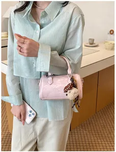 Detail of trendy pink glossy cylindrical handbag with cute plush charm in cozy interior.
