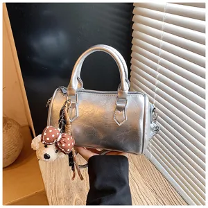 Trendy silver metallic barrel handbag featuring cute bear pendant, stylish retro design.