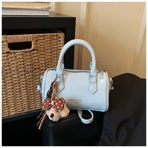 Close-up view of the trendy light blue cylinder handbag featuring a cute bow bear pendant.