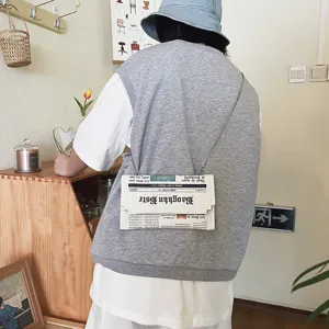 Sac bandoulière enveloppe en similicuir avec motif journal créatif et chaîne élégante détaillée.