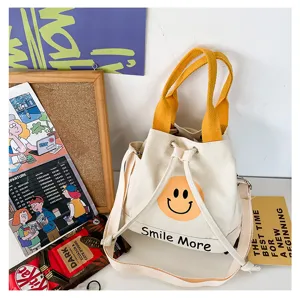 Canvas-Eimerbeutel Detail mit süßem Smiley-Druck, gelben Griffen und verstellbarem Schultergurt.