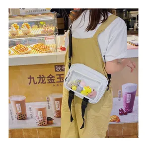 White transparent window crossbody bag detail showing cute plush doll charms and black straps.