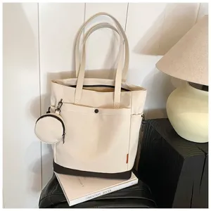Detail view of the beige canvas tote bag with a small coin purse and dark bottom panel.