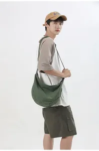 Primer plano de un bolso bandolera de lona verde llevado por un modelo en un estudio.