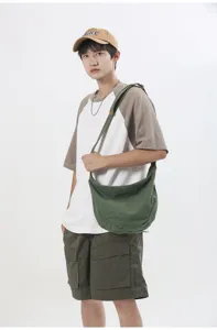 Vista detallada del bolso de hombro de lona verde informal usado por el modelo masculino.