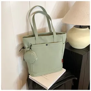 Detail of light green canvas tote bag showing front pocket and small coin purse accessory.