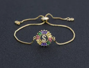 Detailed view of gold plated adjustable bracelet with colorful zirconia circular letter S pendant.