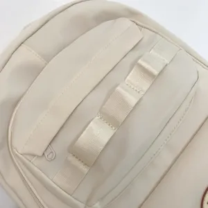 Dettaglio tasca anteriore zaino beige con fettuccia decorativa, design casual e versatile.