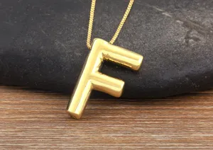 Close-up detail of smooth gold-plated bubble letter F pendant necklace on dark stone surface.