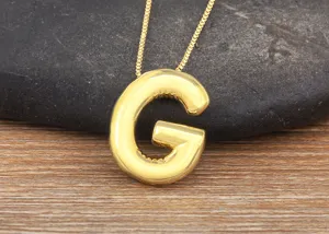 Close-up detail of the 18K gold-plated bubble letter G necklace pendant on stone background.