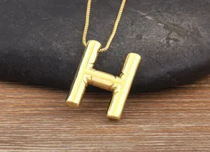 Closeup detail of golden letter H pendant necklace on textured wood background and dark stone.