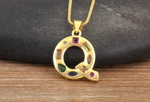 Closeup of gold plated letter Q pendant necklace with colorful cubic zirconia stones on dark rock.