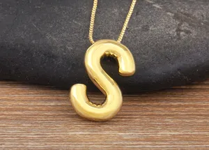 Gold-plated balloon letter S pendant necklace close-up, shiny metallic minimalist jewelry detail.
