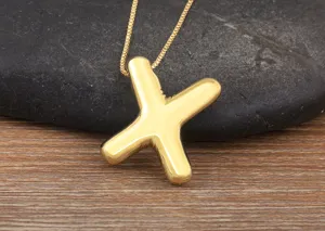 Close-up of gold-plated bubble letter X pendant necklace, smooth surface, minimalist style.