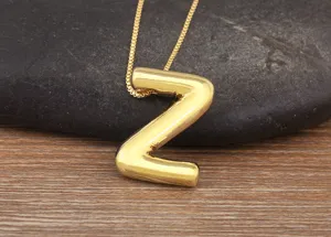 Close-up detail of a shiny gold puff letter Z pendant necklace on dark stone and wood background.