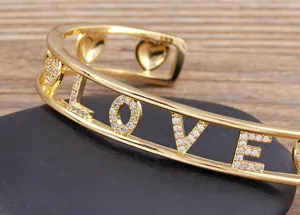 Vergoldeter doppellagiger Love Armreif mit funkelnden Steinen und Herz-Ausschnitten Detail.