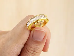 Nahaufnahme des vergoldeten Baguette-Zirkonia-Rings mit baumelndem Herz-Anhänger im Detail.