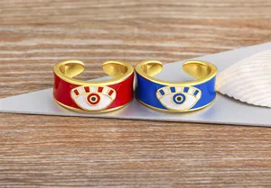 Detailed close-up of trendy gold-plated evil eye open rings in red and blue enamel style.