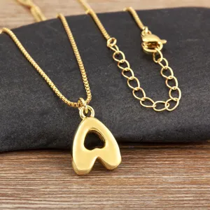 Gros plan détaillé du collier pendentif lettre plaqué or avec chaîne délicate sur pierre sombre.