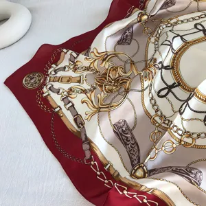 Dettaglio foulard di seta con stampa di catene dorate e cintura su fondo rosso.
