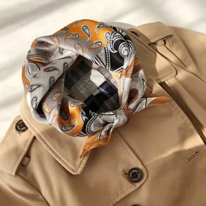 Zijden sjaal detail met elegante geel-grijze paisley print gestyled op een trenchcoat.