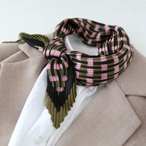 Detailed shot of pleated pink and green plaid satin scarf styled neatly on layered outfit.
