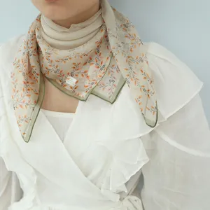 Dettaglio ravvicinato di un foulard in seta leggera con stampa floreale e bordo verde.