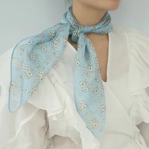 Primo piano dettaglio del foulard quadrato di seta floreale blu al collo, stile estivo.