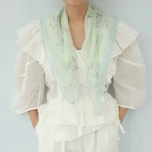 Vista dettagliata del foulard in seta verde chiaro con stampa floreale, elegante.