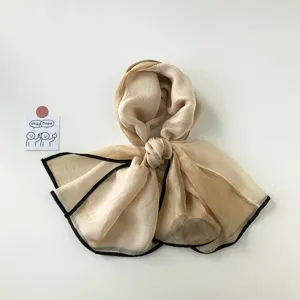 Vista detallada de elegante bufanda de gasa beige con dobladillo negro para estilo chic.