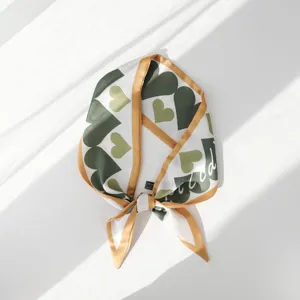 Primo piano dettagliato di un elegante piccolo foulard in seta con cuore verde e bordo dorato.
