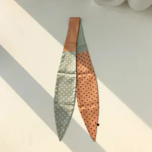 Gros plan sur un très élégant foulard twilly étroit à pois aux couleurs contrastées.