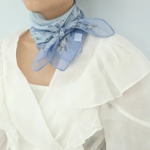 Primo piano di un foulard quadrato in chiffon di seda con stampa floreale blu al collo.