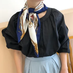 Detail view of a luxury silk square scarf featuring classic carriage and chain prints, worn elegantly.