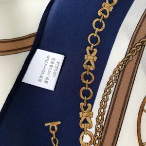 Close-up of luxury silk scarf fabric detail, showing exquisite chain print and wash label.