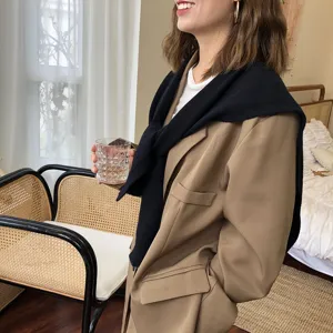 Gestrickter Schal ueber khakifarbenem Blazer im gemuetlichen Schlafzimmer, Herbst-Modedetail.