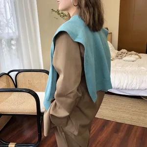 Nahaufnahme des stilvollen blauen Strickshawls über braunem Blazer im gemütlichen Schlafzimmer.