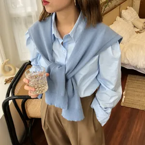 Detailaufnahme des blauen Strickschals kombiniert mit Hemd im gemütlichen Innenszenario.