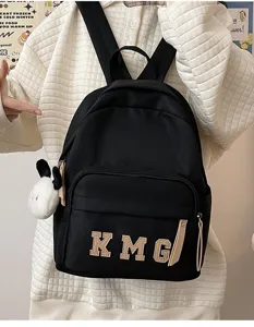 Vista detallada de una linda mochila negra para niños con parche de letras y colgante.