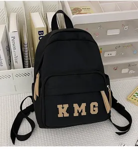 Detalle de la mochila escolar negra con parches de cuero en la letra y bolsillo con cremallera.